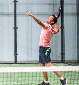 Man playing padel in a green grass padel court indoor behind the net